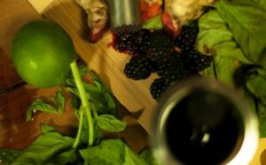 Blackberry and other fresh ingredients on a wooden board next to a black drink
