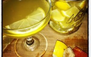 Martini glass with a yellow liquid and a slice of lemon next to a full glass of lemon juice