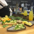 Fresh lemon slices and other cocktail ingredients plated on a wooden table next to bottles of cocktail mixers